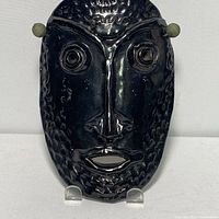 Front view of black stoneware ceramic mask with glossy finish and textured facial features