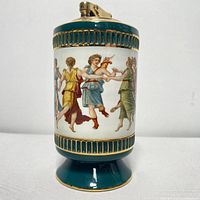 Front view of porcelain lighter showing dancing maiden illustration in green, yellow, blue, and red costumes with green base and brass top lighter mechanism.