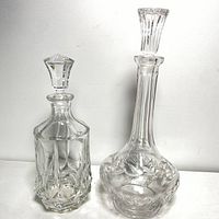 Photo of two etched crystal decanters side by side, clear background showing geometric and floral designs.