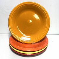 Three Fiesta ceramic dinner plates stacked, showing top plate is orange, with yellow and red plates underneath.
