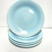Four sky blue Fiesta Ware dinner plates stacked with one plate displayed upright showing the concentric rings design.