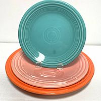 Front view of teal side plate on top of pink luncheon plate and orange dinner plate, showing color and design.