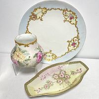 Overview of all three items: large display plate with gold and pink floral designs, footed planter with chrysanthemum flowers and gold trim, and Nippon trinkets dish with pink flowers and gold border.