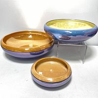 Three Noritake lusterware nesting bowls in blue and purple with yellow interior, displayed side by side with smallest in front, medium in middle, largest in back elevated.