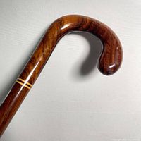 Close-up image of the curved hook handle of the polished mahogany cane showing wood grain and two lighter inlaid rings.
