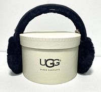 Black UGG wired sheepskin earmuffs displayed on top of original round UGG box.