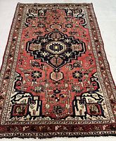 Full view of red field rug with central navy blue medallion and ivory borders