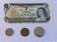 Canadian one dollar bill from 1973 displayed above three coins of varying sizes.