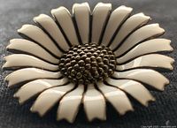 Close-up photo of the front of a sterling silver and white enamel daisy floral pin showing white petals with silver outlines and a textured center.
