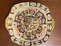 Top-down photo showing Aynsley teacup, saucer stacked and Royal Albert plate beneath, displaying their colorful floral and geometric pattern with gold accents.