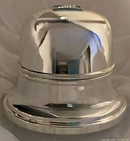 Close-up photo of polished silver plated bell-shaped box, showing smooth curved surface reflecting surroundings.