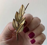 Front view of the brooch held in hand showing four gold-tone textured leaves design.