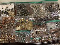 Multiple resealable bags filled with assorted costume jewelry such as necklaces, bracelets, and earrings, arranged on a surface.