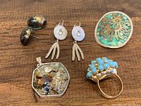 Full lot of mixed jewelry including Jackie Spector pewter earrings, silver turquoise pin, turquoise-colored gold-tone ring, vintage pendant, and blue/gold earrings shown on wooden background.