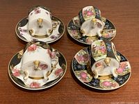 Four demitasse cups and matching saucers shown upside down to display tri-foot design and floral handpainted motifs.
