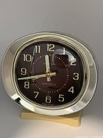 Front view of the vintage Westclox Baby Ben alarm clock with brown face, gold-tone numerals and hands, cream-colored exterior, and gold-tone outer band.