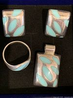 Photo of front side of rectangular sterling silver earrings, pendant, and ring featuring blue enamel inlays arranged in a leaf pattern.