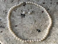 Full view of pearl necklace and matching pearl stud earrings laid on a stone surface.