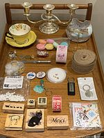 Full view of the lot items arranged on a wooden chair, including silver plated candelabra, teacup set, bow, ribbons, stickers, keychains, stamps, and other small items.