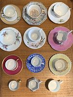 Full lot of 10 assorted vintage demitasse cups and saucers displayed on wooden surface, various colors and styles.