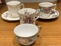 Four demitasse cups with three saucers, floral patterns and gold trim, on wooden surface.