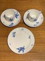 Top-down view of two bone china cups and saucers with blue bird designs and one plate on wooden surface.