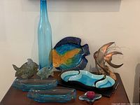 Overview of lot showing tall blue glass bottle/vase, bright fish ceramic dish, two glass starfish candle holders, copper fish sculpture, and MCM Anchor Hocking blue colonial serving dishes.