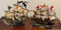 Two vintage model ships displayed side by side on a flat surface. Left ship is the Santa Maria with distinct sail markings; right ship is Fragata Espanola.