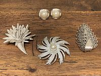 All four pieces including three silver tone brooches and one pair of faux pearl rhinestone earrings on wooden surface