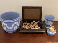 Four items displayed on wood surface: wooden keepsake box open with sewing spools inside, Wedgwood-style pale blue planter with white relief decoration, Wedgwood mini vase, and Wedgwood-style lighter.