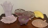 Front view of assorted vintage pink and yellow glass decorative pieces including two frosted pink lotus/waterlily bud vases, a pink ribbon vase, pink floral candy dish, pink apple-shaped candy dish, and a yellow napkin holder