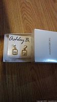Photo of brand new Ashley B. The Broadway earrings in original box, showing gold-tone metal square drop design with clear rhinestones and attached stud with clear rhinestone.