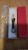 Fossil women's watch with brown crocodile pattern leather strap inside white box, accompanied by bubble wrap and a red Robisons-May box with white heart pattern resting on a wooden floor.