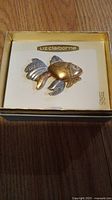 Fish-shaped pendant in gold and silver tones inside a Liz Claiborne branded box.