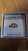 Photo showing a sterling silver heart pendant in its original branded box labeled "The Millennium Heart" with amfAR support message.