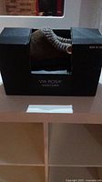 Front view of Via Rosa slippers in packaging showing size and knit fabric design with button accent.
