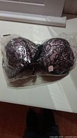 Photo showing the front view of the black Victoria's Secret bra with pink lace overlay, enclosed in clear plastic packaging, label visible under the packaging.