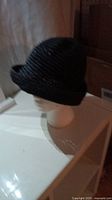 Front angle view of black woven woman’s hat on mannequin head, showing folded brim and rounded crown.