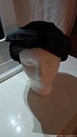 Front view of the black woman's hat with large bow on side displayed on mannequin head.