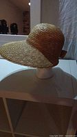Side view of tan woven straw hat with a broad brim, displayed on a white mannequin head.
