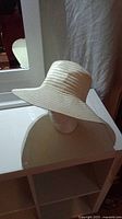 Side view of the white straw hat positioned on a mannequin head, showing the curved wide brim and woven texture.