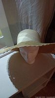 Front angle of the wide-brim straw hat on a mannequin head showing the round crown and lace trimmed brim.