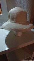 Front view of the beige woven straw women's sun hat placed on a display stand showing the rounded crown and brim shape.