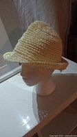 Side view of the women's woven straw hat on a white mannequin head showing the rolled brim edge and overall shape