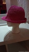 Side view of a pink crochet women's hat on a mannequin head showing the small curled brim and rounded crown