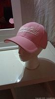 Front side view of pink baseball cap on white mannequin head indoors