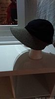 Photo of women's hat showing black fabric crown and wide woven natural fiber brim on mannequin head.