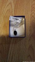 Photo of a brand new women's necklace with silver chain and black oval pendant displayed in a small blue box on a wooden surface.