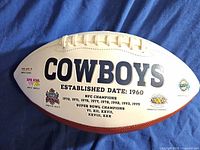 Front panel of football with 'COWBOYS' text and listed historical NFC and Super Bowl championships including years and Super Bowl Roman numerals.