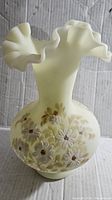 Front view of yellow custard uranium glass vase with painted white flowers and ruffled lip.